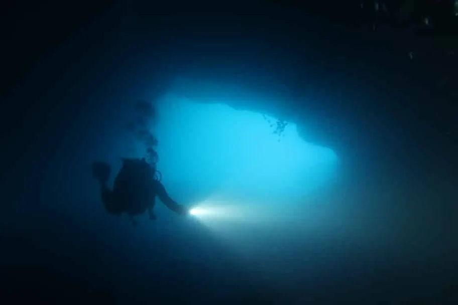 Plongeur éclairant l’entrée d’une grotte sous-marine
